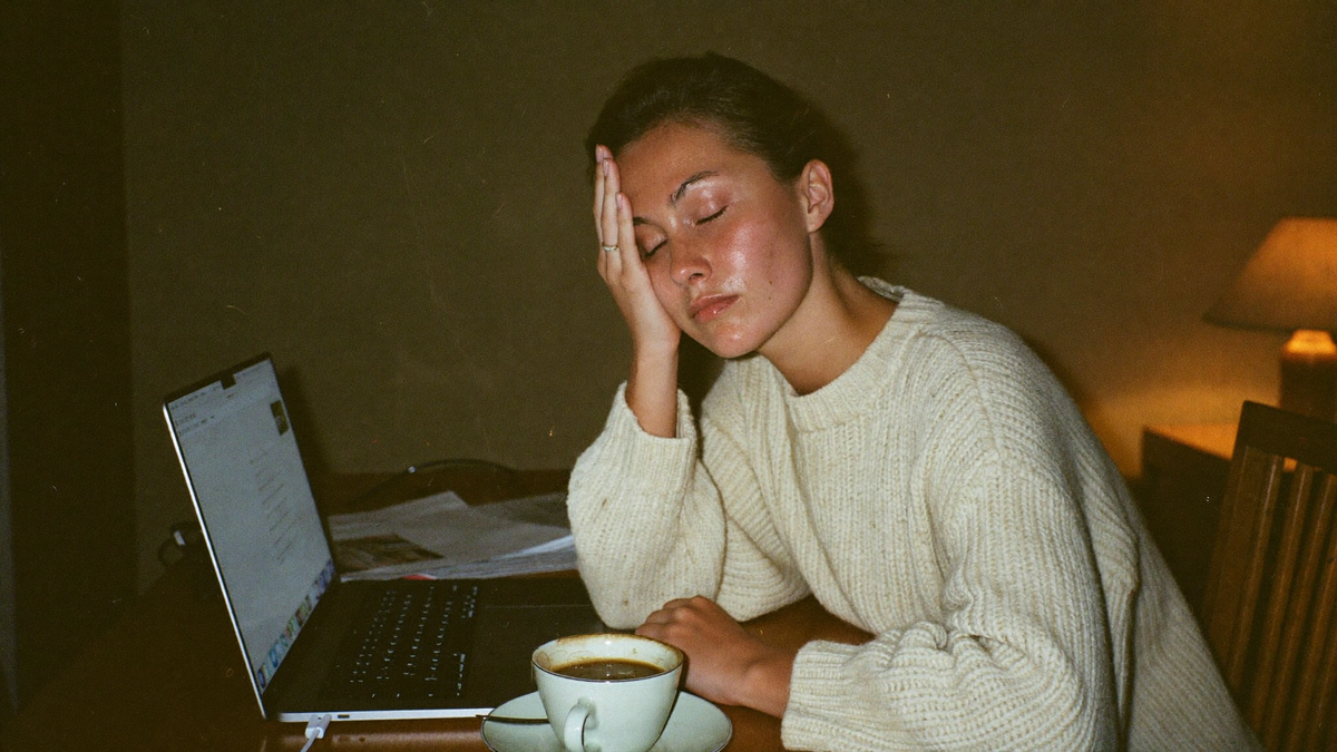 Unavená žena večer u notebooku drží ruku u spánku